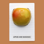 The Apples and Banana symbol with a red faux apple embedded in the center. Labeled "Apples & Banana Apple" in black font at the bottom of symbol on white backing. The background of the symbol is white.