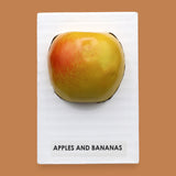 The Apples and Banana symbol with a red faux apple embedded in the center. Labeled "Apples & Banana Apple" in black font at the bottom of symbol on white backing. The background of the symbol is white.