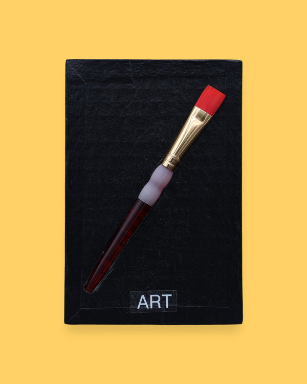 The Art symbol is crafted with a durable plastic paintbrush, the paintbrush handle color may vary. The paintbrush is embedded diagonally. Labeled "Art" in black font at the bottom of symbol on white backing. For black high contrast Art symbol the backing is black with a varied high contrast colored paintbrush. 