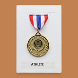 The Award symbol is circular gold plated medal embedded in the center position on a white background with red, white, blue ribbon fabric at the top of the award medal. Labeled 