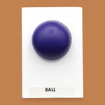 The Ball symbol with a small navy blue rubber ball embedded in the center. Labeled "Ball" in black font at the bottom of symbol on white backing. The background of the symbol is white.