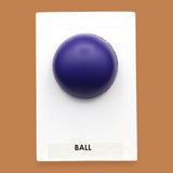 The Ball symbol with a small navy blue rubber ball embedded in the center. Labeled "Ball" in black font at the bottom of symbol on white backing. The background of the symbol is white.