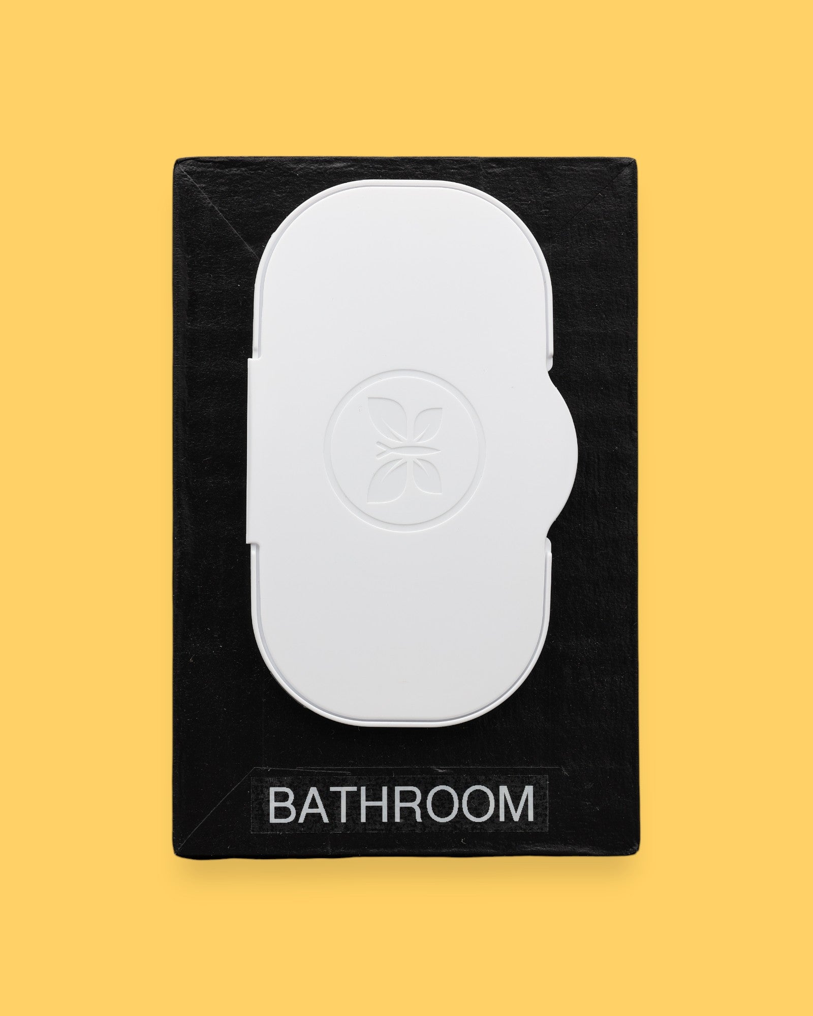 The Bathroom-wipes-lid symbol has a lid of freshwiped embedded vertically in the center of the symbol. Labeled "Bathroom" in black font at the bottom of symbol on white backing. The background of the symbol is white.