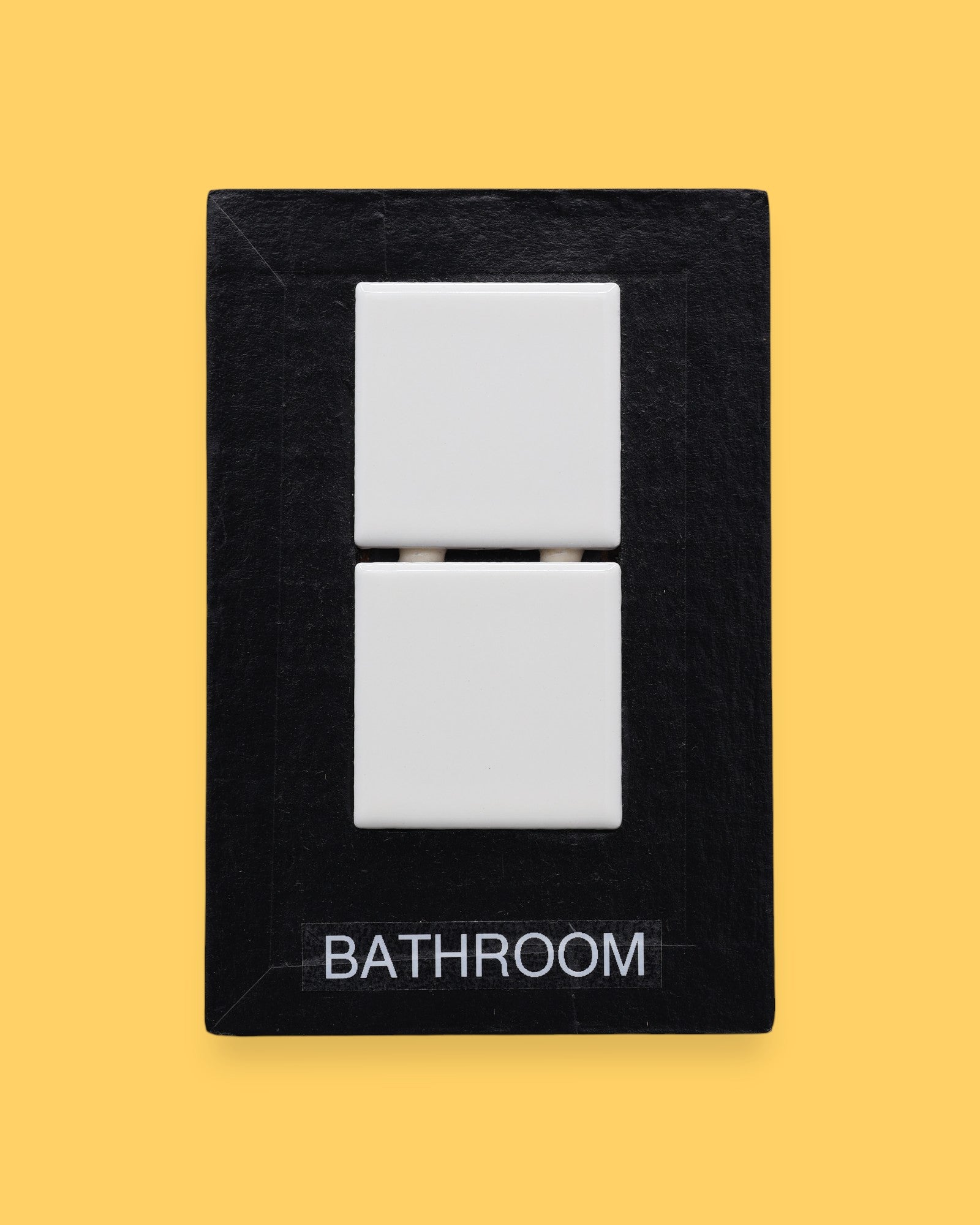 The Bathroom-tile symbol has two square, white, ceramic tiles are embedded vertically in the center of the card. Labeled "Bathroom" in black font on white backing. The background of the symbol is white.