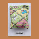 The Bed Time symbol with a piece of comforter fabric embedded in the center. Labeled "Bed Time" in black font at the bottom of symbol on white backing. The background of the symbol is white.
