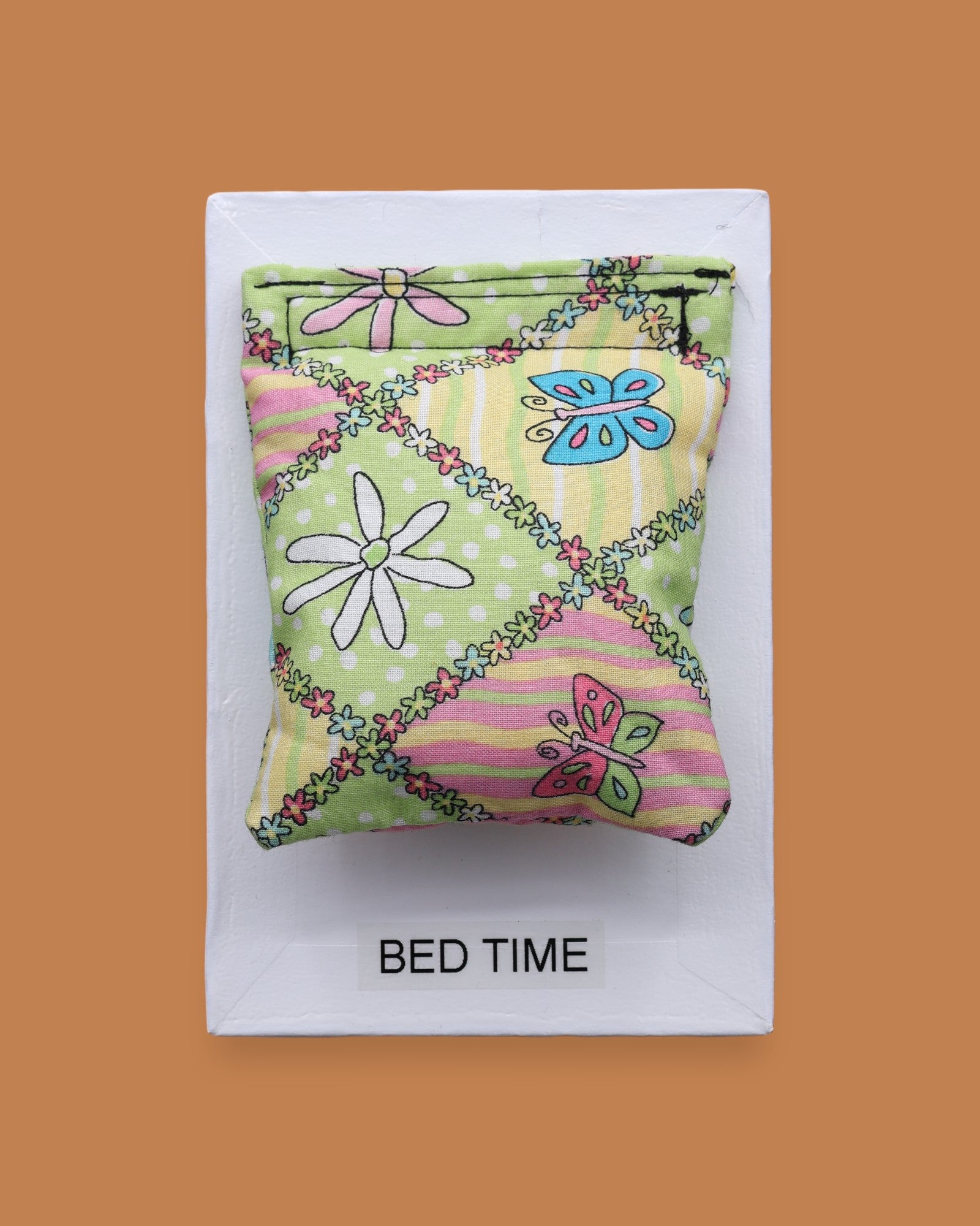 The Bed Time symbol with a piece of comforter fabric embedded in the center. Labeled "Bed Time" in black font at the bottom of symbol on white backing. The background of the symbol is white.