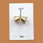 The Bell with two small golden-plated metal bells embedded sided by side with a green interlocked wire holding the bells together. Labeled "Bell" in black font at the bottom of symbol on white backing. The background of the symbol is white.