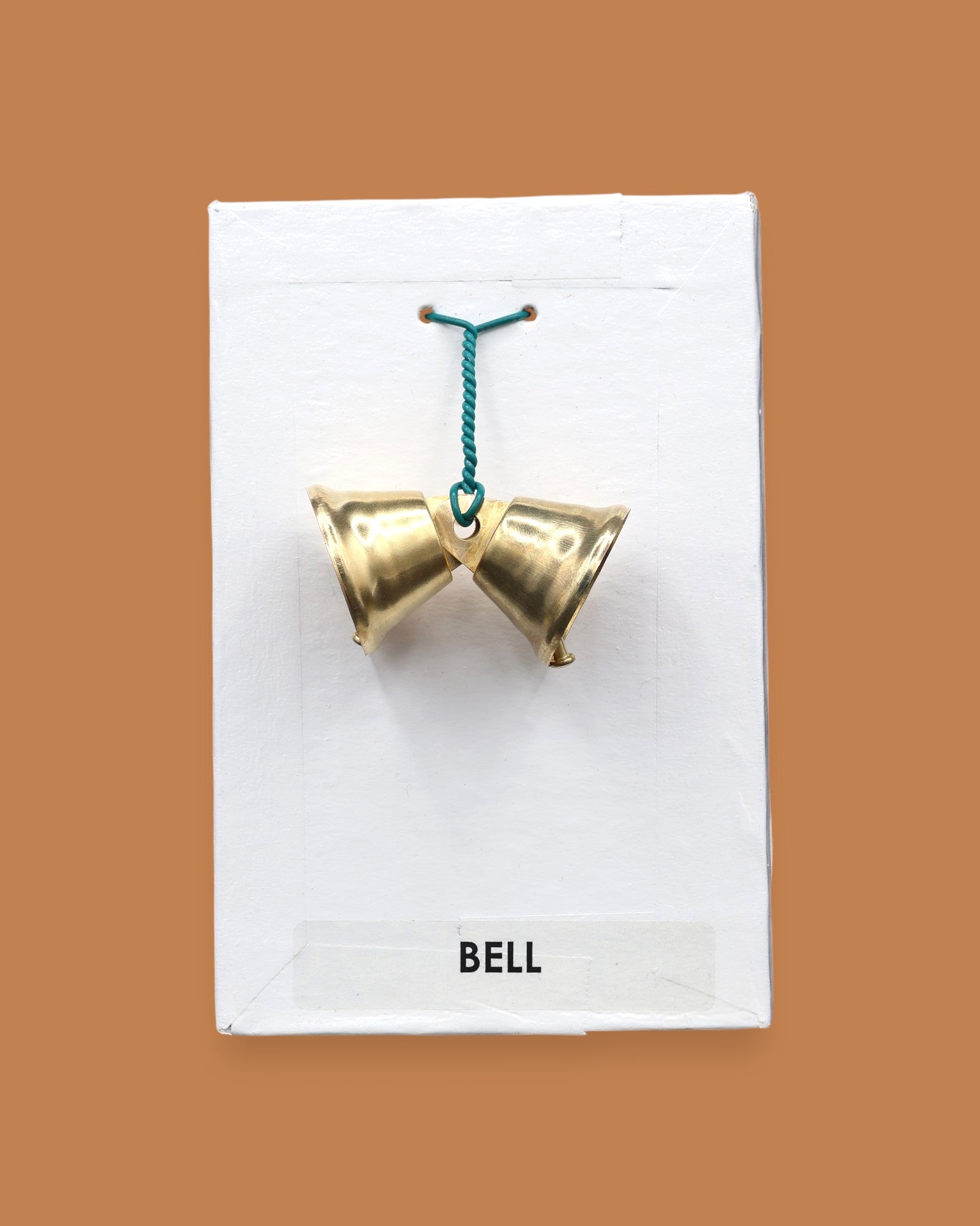 The Bell with two small golden-plated metal bells embedded sided by side with a green interlocked wire holding the bells together. Labeled "Bell" in black font at the bottom of symbol on white backing. The background of the symbol is white.