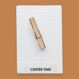 The Center Time symbol consists of a wooden clothespin embedded vertically in the center. Labeled "Center Time: in black font on white backing at the bottom of the symbol. The background of the symbol is white. 