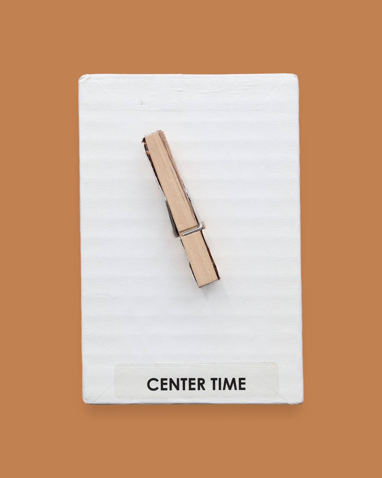 The Center Time symbol consists of a wooden clothespin embedded vertically in the center. Labeled "Center Time: in black font on white backing at the bottom of the symbol. The background of the symbol is white. 