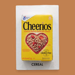 The Breakfast Loose Cereal symbol a carefully prepared blend of hot glue and toasted O’s cereal, formed into a circular shape, is embedded at the center of the card, creating a visually engaging and tactile focal point. The card can be customized, using a black backing for increased contrast.