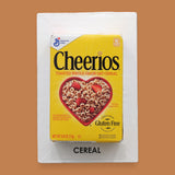 The Breakfast Loose Cereal symbol a carefully prepared blend of hot glue and toasted O’s cereal, formed into a circular shape, is embedded at the center of the card, creating a visually engaging and tactile focal point. The card can be customized, using a black backing for increased contrast.
