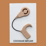 The Cochlear Implant symbol is 3D printed on a tan or sand colored filament on a white backing. For visual high contrast the Cochlear Implant could be printed in high contrast color of choice. 
