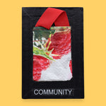 The Community symobl has a small textured bag with red raspberries printed on it, attached by a red strap. Labeled "Community" with white font at the bottom of symbol on clear backing. The background of the symbol is black.