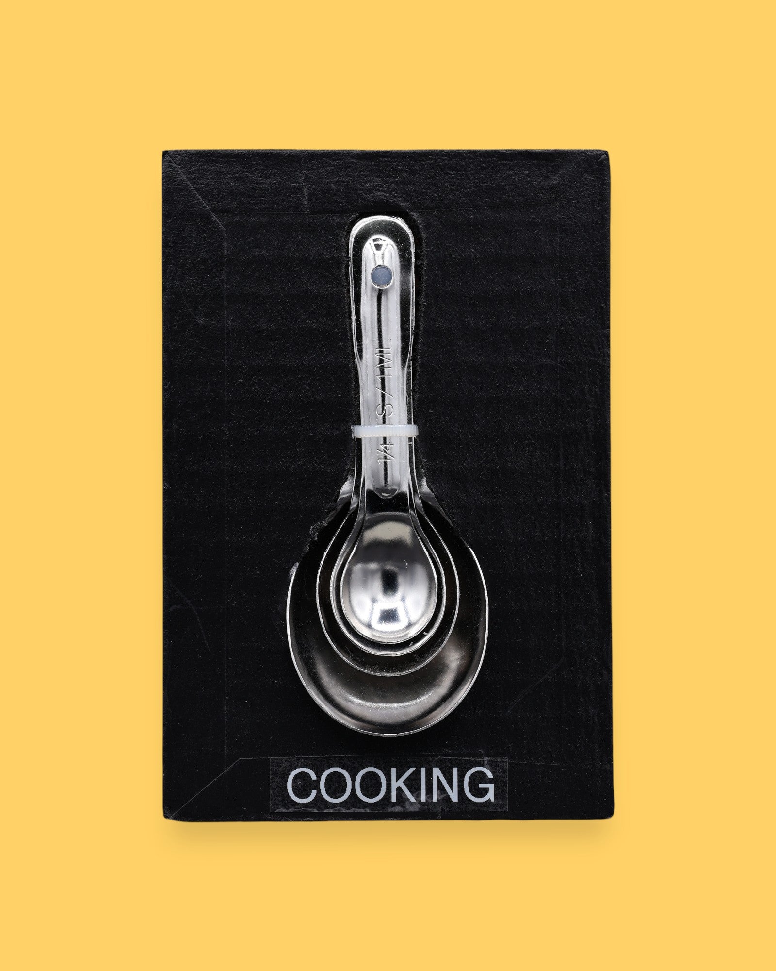 The Cooking symbol has cooking/measuring spoons embedded vertically in the center. Labeled "Cooking" in black font and white backing at the bottom of symbol.. The background of the card is white.