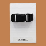 The Dismissal symbol with a black closed buckle embedded in the center horizontally. Labeled "Dismissal" in black font on white backing. The background of the symbol is white. 