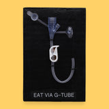 The Eat by mouth Spoon high contrast tactile symbol with a silver spoon embedded in the center. Labeled "Eat" in white font on clear backing at the bottom of the symbol. The background of the symbol is black. 