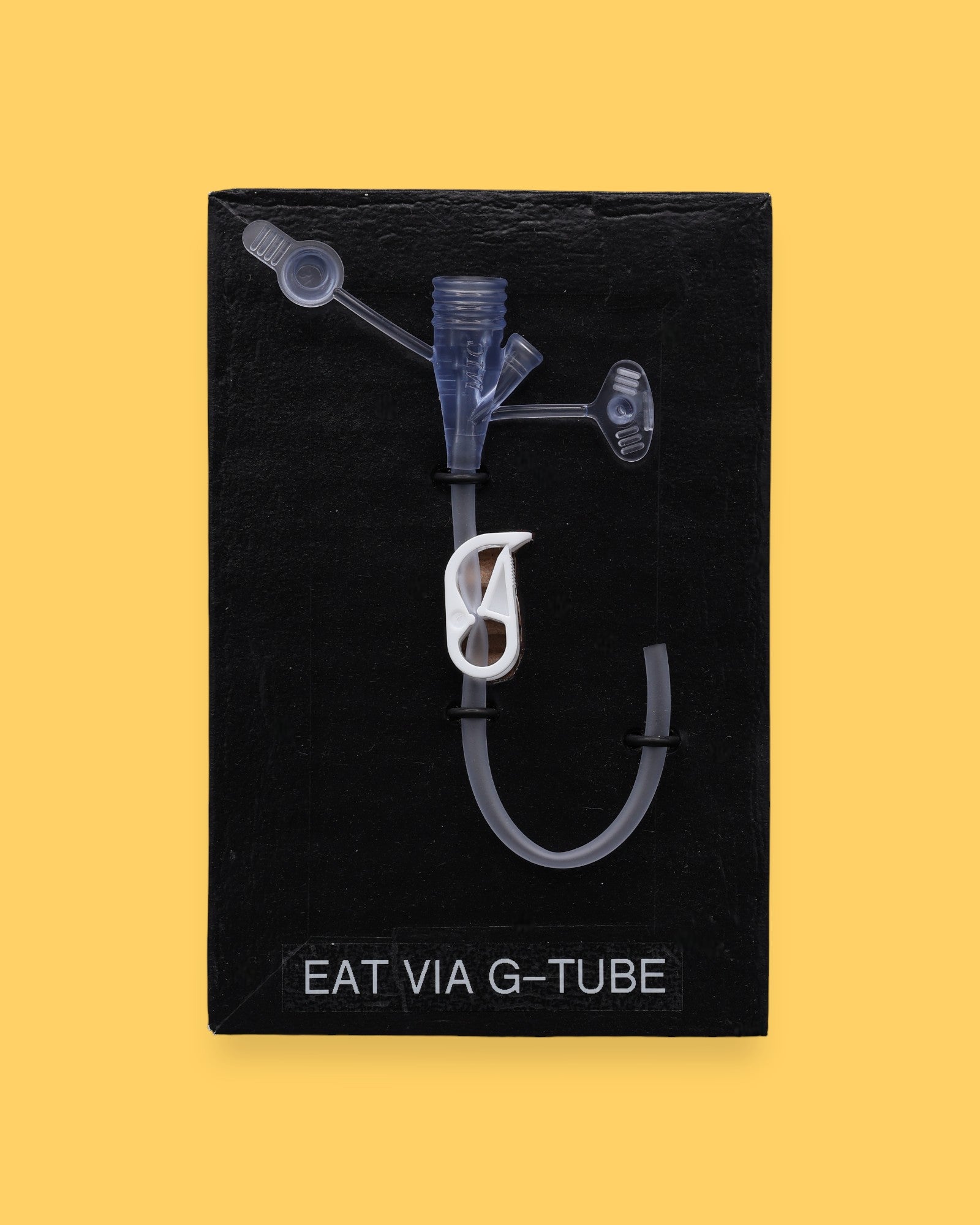 The Eat by mouth Spoon high contrast tactile symbol with a silver spoon embedded in the center. Labeled "Eat" in white font on clear backing at the bottom of the symbol. The background of the symbol is black. 