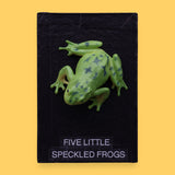 The Five Little Speckled Frogs symbol is a 3" frog toy figure embedded in the center of the cue on top of a recessed wooden base. These plastic frogs come in a variety of designs and colors. The background of the card is black.