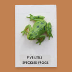 The Five Little Speckled Frogs symbol is a 3" frog toy figure embedded in the center of the cue on top of a recessed wooden base. These plastic frogs come in a variety of designs and colors. The background of the card is white.