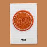 The Fruit symobl has a synthetic orange slice is embedded at the center. Labeled "Fruit" in black font on white backing at the bottom of the symbol. The background of the symbol is white. 