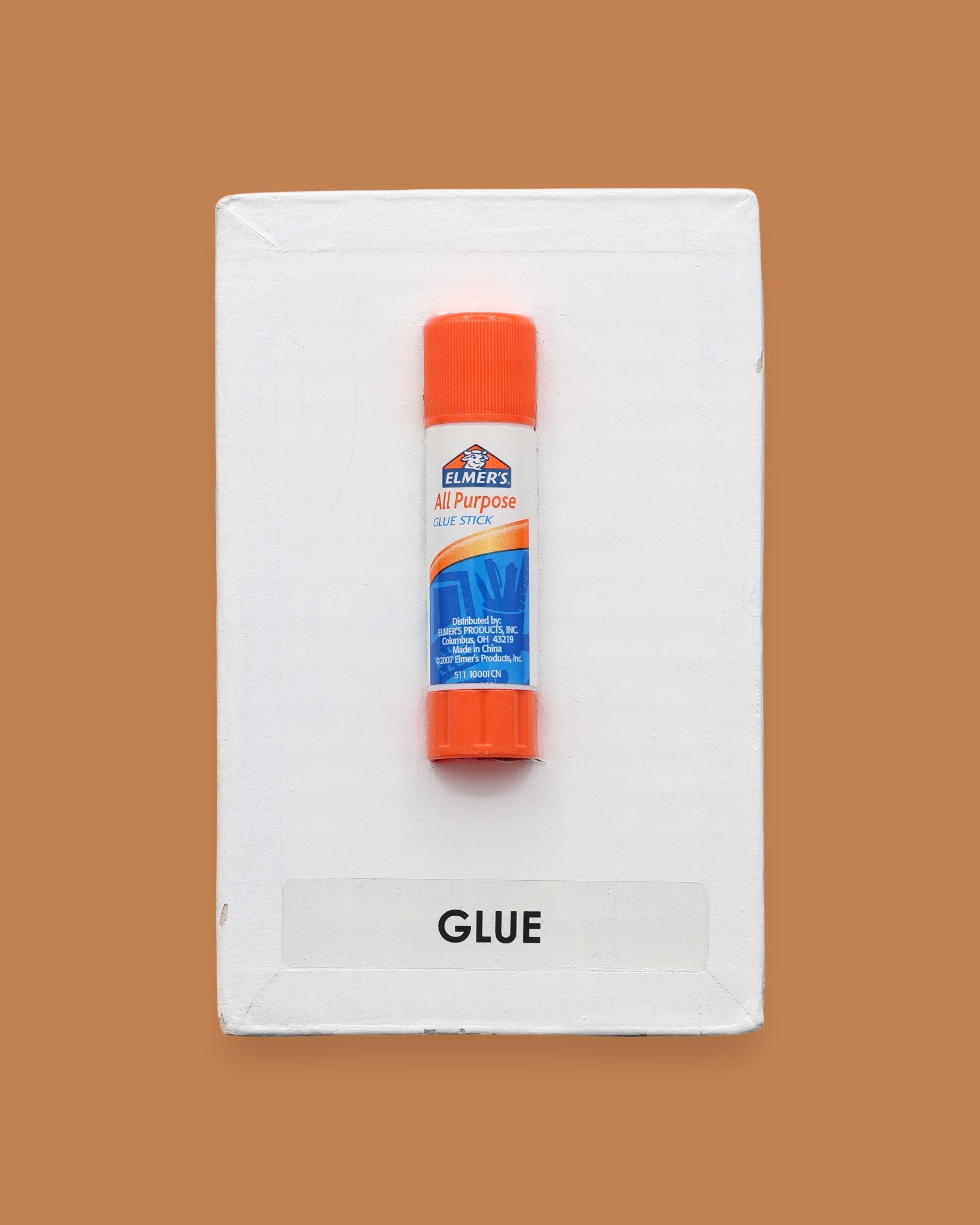 The Glue Stick is blue, orange and white and embedded in the center. Labeled "Glue Stick" in black font on white backing at the bottom of symbol. The background of the symbol is white.