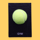 The Gym symbol has a bright yellow tennis ball is centered on a white rectangular surface against a white background. Labeled "Gym" in black font on white backing at the bottom of symbol. The background of the symbol is white.