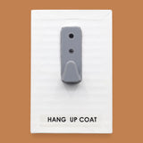 The Hang Up Coat symbol consists of a gray coat hook embedded vertically. Labeled "Hang Up Coat" in black font on white backing at the bottom of the symbol. The background of the symbol is white. 