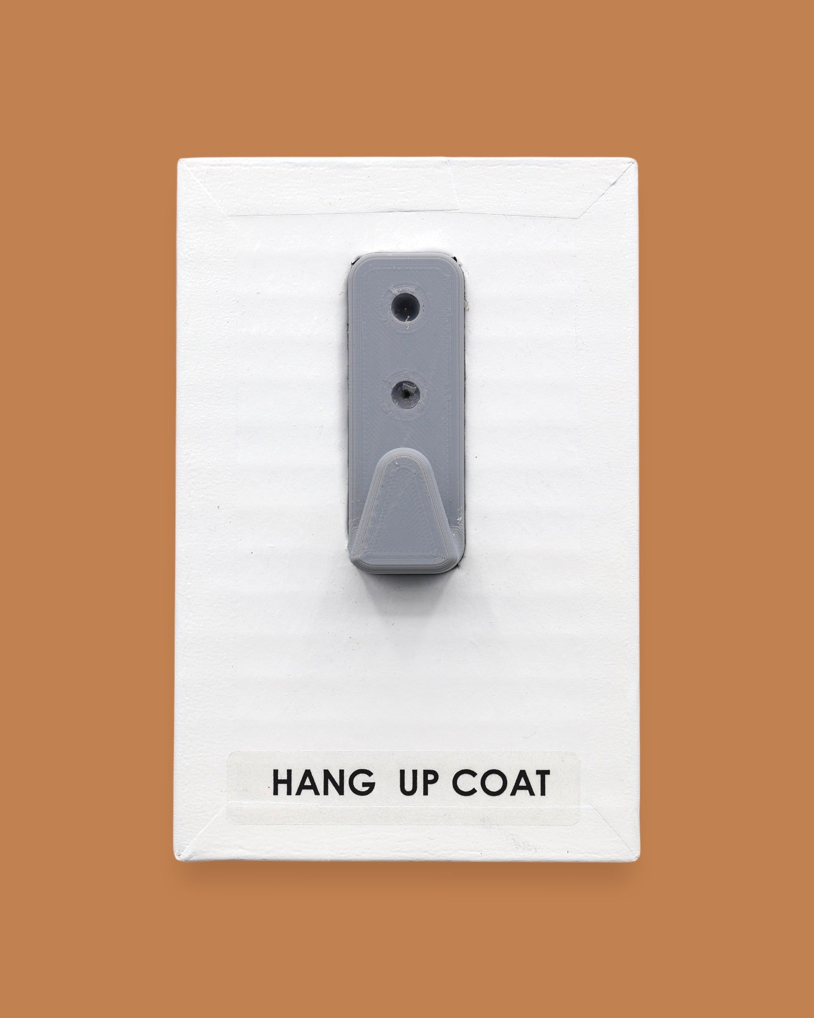 The Hang Up Coat symbol consists of a gray coat hook embedded vertically. Labeled "Hang Up Coat" in black font on white backing at the bottom of the symbol. The background of the symbol is white. 
