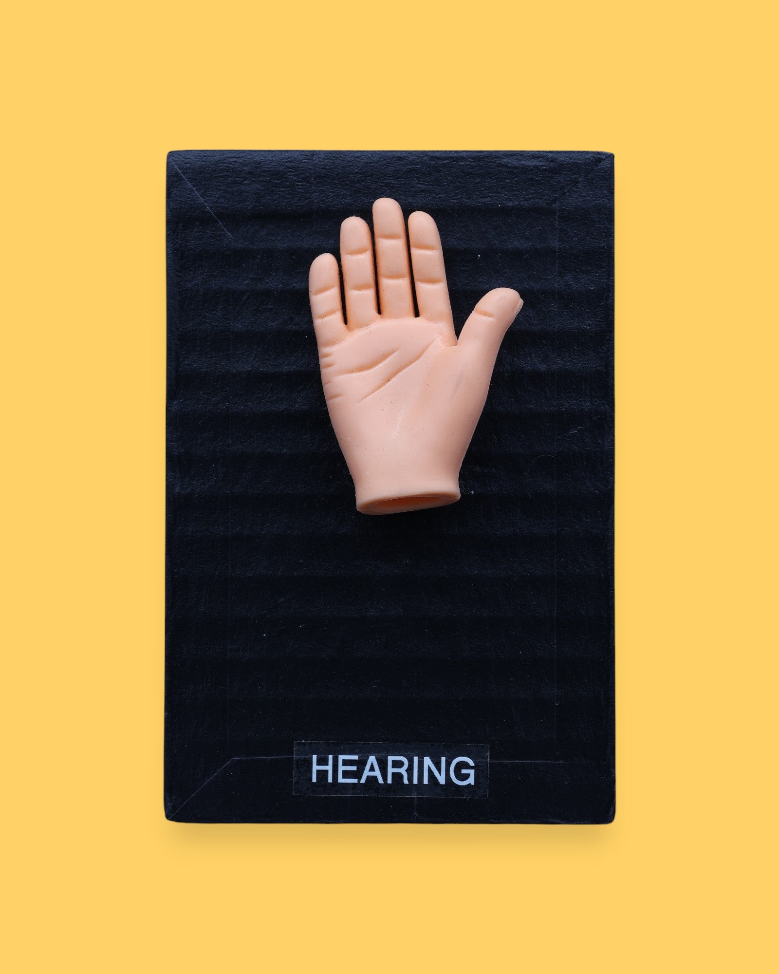 The Hearing-hand high contrast tactile symbol has embedded in the center a small hand shape on a black background. Labeled "Hearing-hand" in white font and clear backing.