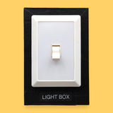 The Light Box high contrast tactile symbol with a bright rectangular flickable light switch. Labeled "Light Box" in white font at the bottom of symbol on clear backing. The background of the symbol is black. 