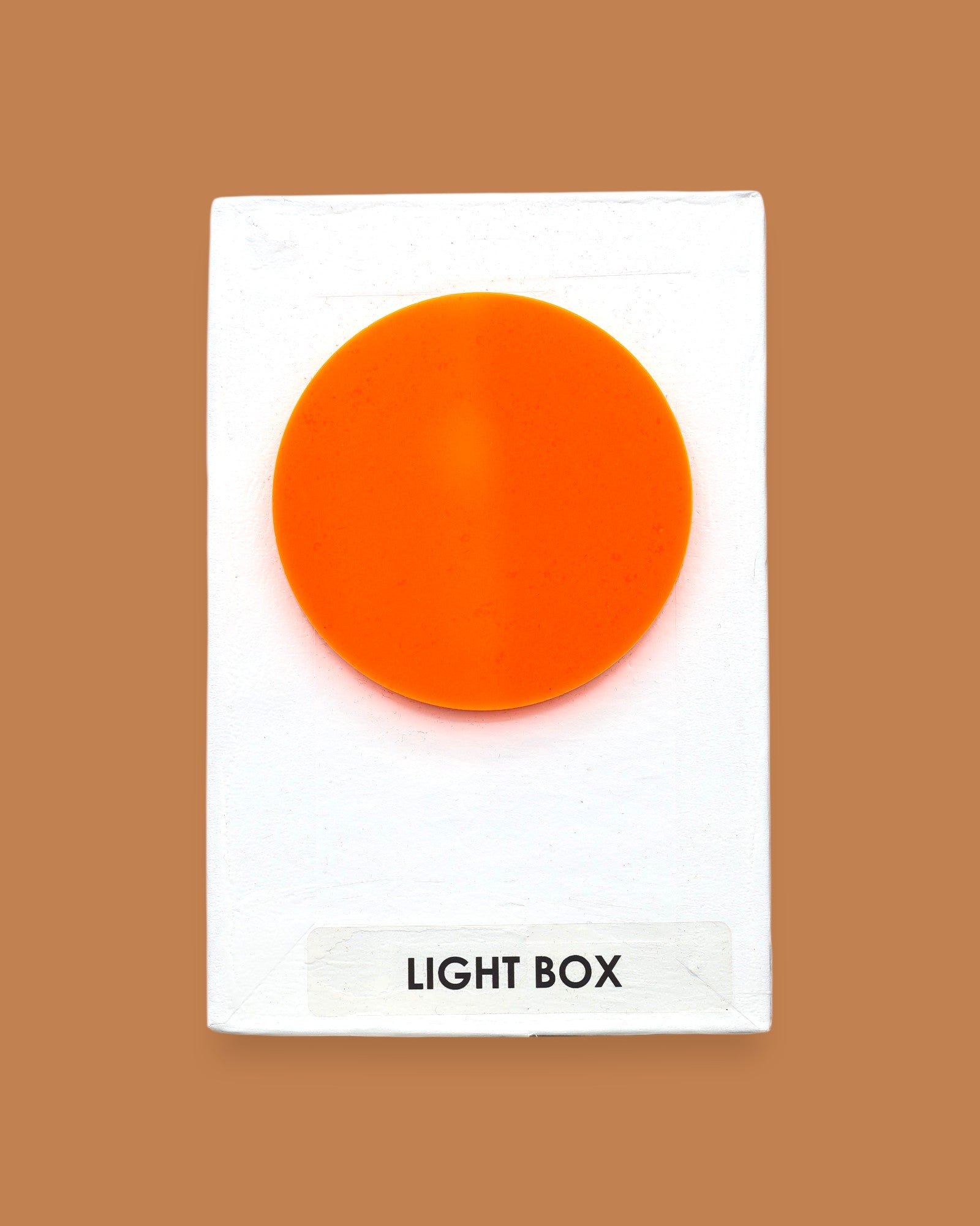 The Light Box Plastic Shape symbol with a smooth circular piece embedded in the center. Labeled "Light Box" in black font on white backing at the bottom of the symbol. The background of the symbol is white. 
