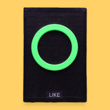 The Like high contrast tactile symbol card for Like with a neon 3D printed PLA filament green ring embedded in the center. Labeled "Like" in white font at the bottom of symbol on clear backing. The background of the symbol is black. 