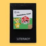 The Literacy symbol has mini children's board book titled "Let's Make Lunch" with a cartoon red bird holding corn. Background shows a picnic setting. Labeled "Literacy" in black font on white backing at the bottom of symbol . The background of the symbol is white.