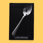 The Lunchroom symbol has a metal spoon embedded in the center. Labeled "Lunchroom" in black font on white backing at the bottom of symbol. The background of the symbol is white.