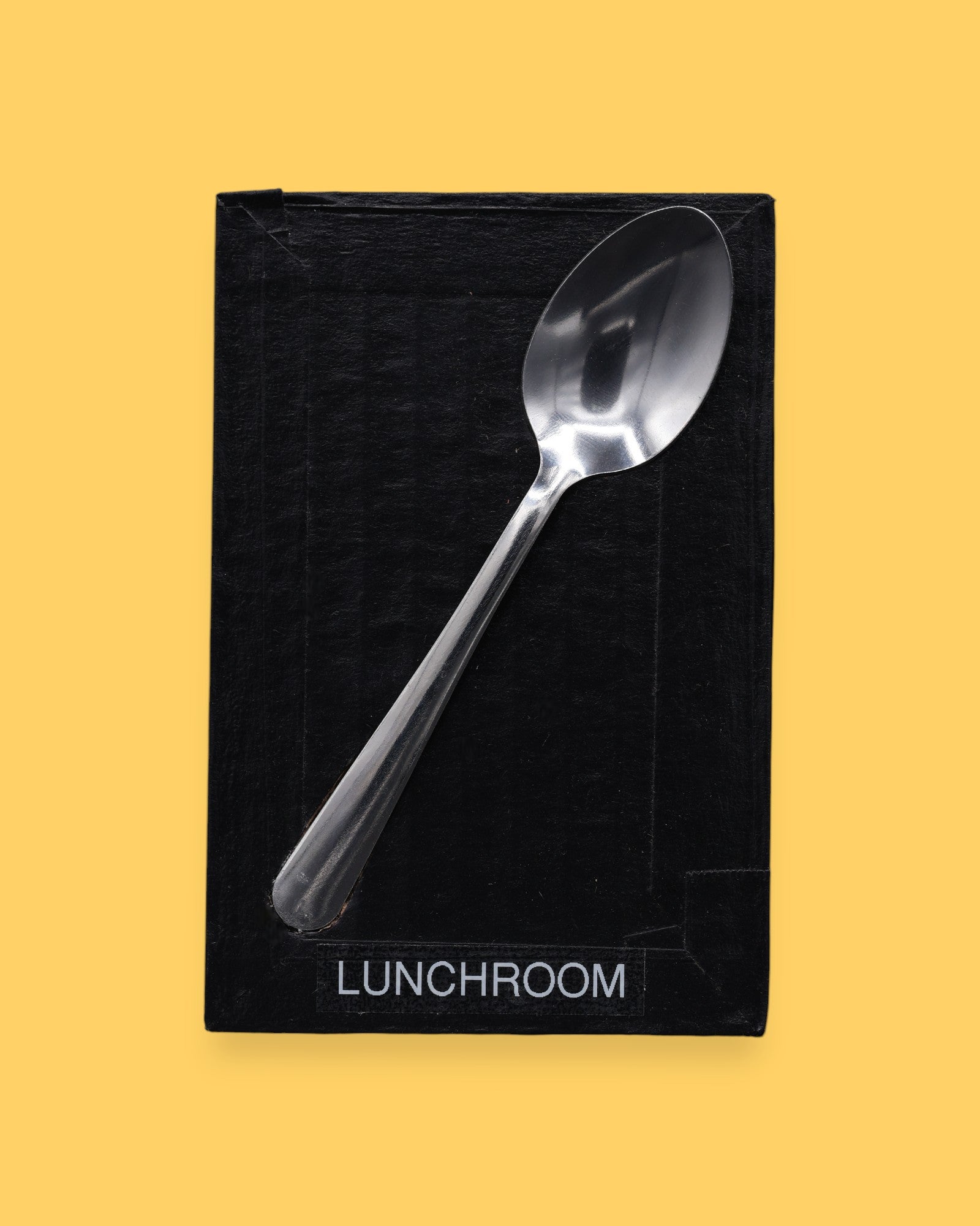 The Lunchroom symbol has a metal spoon embedded in the center. Labeled "Lunchroom" in black font on white backing at the bottom of symbol. The background of the symbol is white.