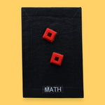 The Mat Time high contrast tactile symbol with a maroon colored fabric filled with batton embedded in the center. Labeled "Mat Time" in white font on clear backing at the bottom of the symbol. The background is black. 