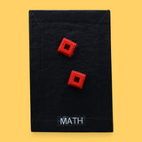 The Mat Time high contrast tactile symbol with a maroon colored fabric filled with batton embedded in the center. Labeled "Mat Time" in white font on clear backing at the bottom of the symbol. The background is black. 
