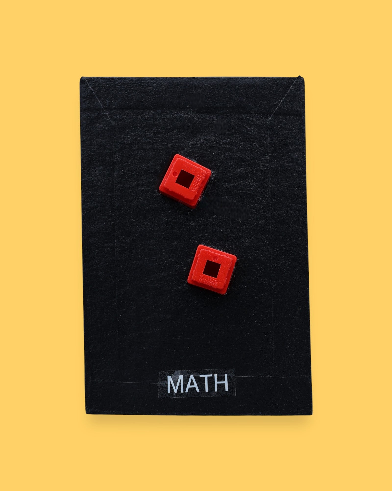 The Mat Time high contrast tactile symbol with a maroon colored fabric filled with batton embedded in the center. Labeled "Mat Time" in white font on clear backing at the bottom of the symbol. The background is black. 