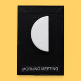 The Morning Meeting high contrast tactile symbol with a half-circle shape embedded in the center. Labeled "Morning Meeting" in white font on clear backing at the bottom of the symbol. The background of the symbol is black. 