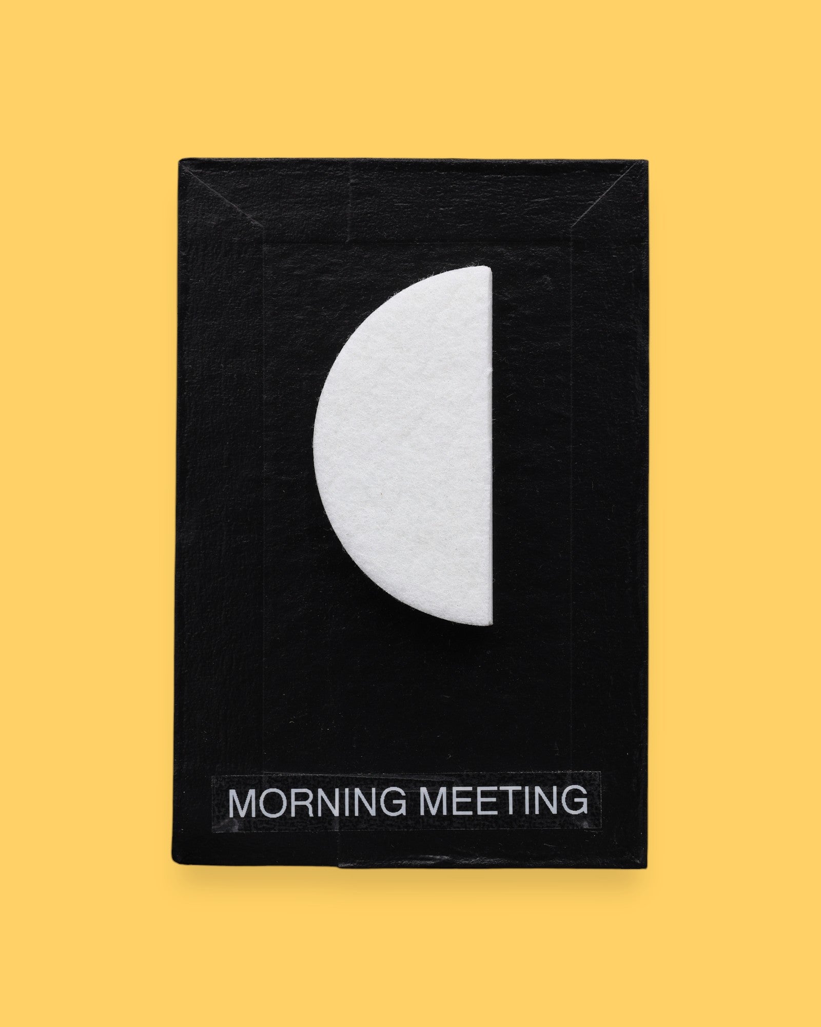 The Morning Meeting high contrast tactile symbol with a half-circle shape embedded in the center. Labeled "Morning Meeting" in white font on clear backing at the bottom of the symbol. The background of the symbol is black. 