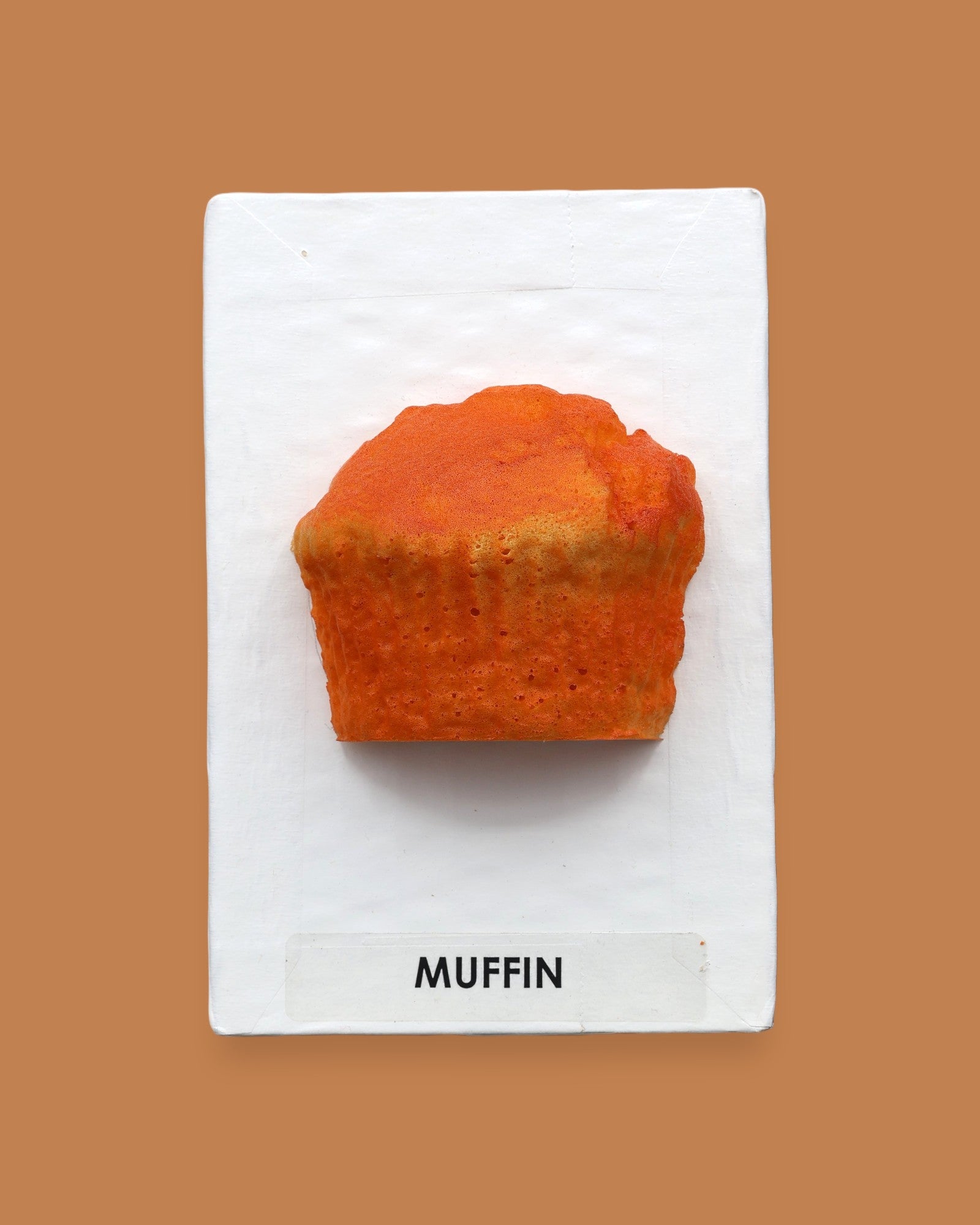 The Muffin symbol embedded with a tan colored faux food muffin. Labeled "Muffin" in black font on white backing at the bottom of the symbol. The background of the symbol is white. 