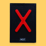 The Not high contrast tactile symbol with a bright red 3D printed filament X  embedded in the center. Labeled "Not" in white font on clear backing. The background of the symbol is black. 