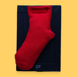 The OT Sock high contrast tactile symbol has a red cotton toddler sized sock embedded in the center with batton filling. Labeled "OT" in white font on clear backing at the bottom of the symbol. The background of the symbol is black.  