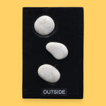 The Outside symbol consists of 3 gray colored real rocks It is composed of real rocks securely embedded diagnolly. Labeled "Outside" in black font and white backing at the bottom of symbol . The background of the symbol is white. 