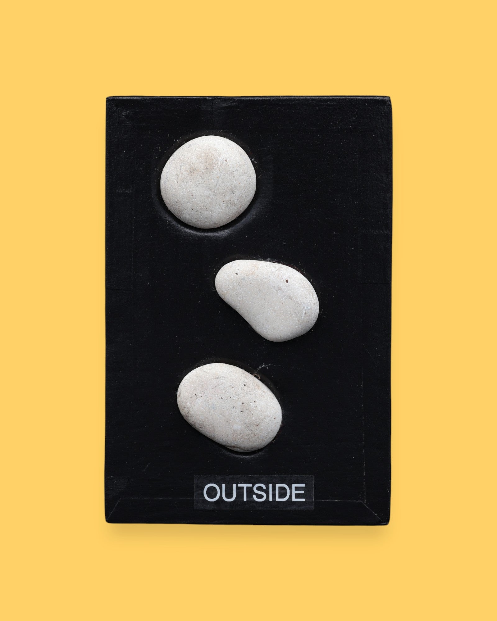 The Outside symbol consists of 3 gray colored real rocks It is composed of real rocks securely embedded diagnolly. Labeled "Outside" in black font and white backing at the bottom of symbol . The background of the symbol is white. 