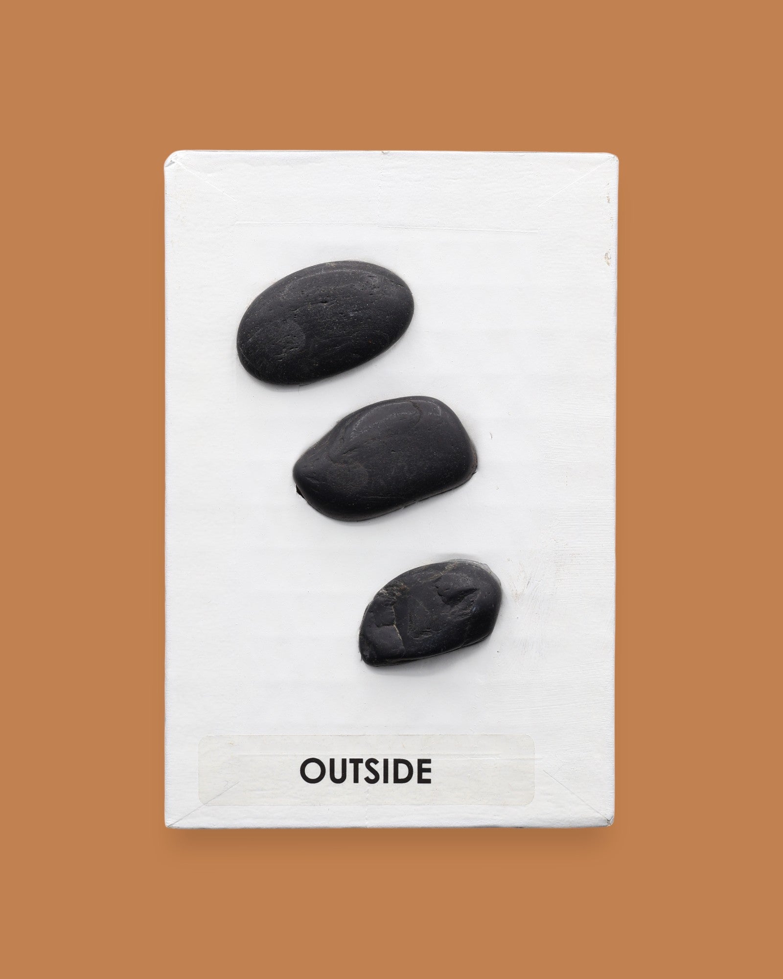 The Outside symbol consists of 3 gray colored real rocks It is composed of real rocks securely embedded diagnolly. Labeled "Outside" in black font and white backing at the bottom of symbol . The background of the symbol is white. 