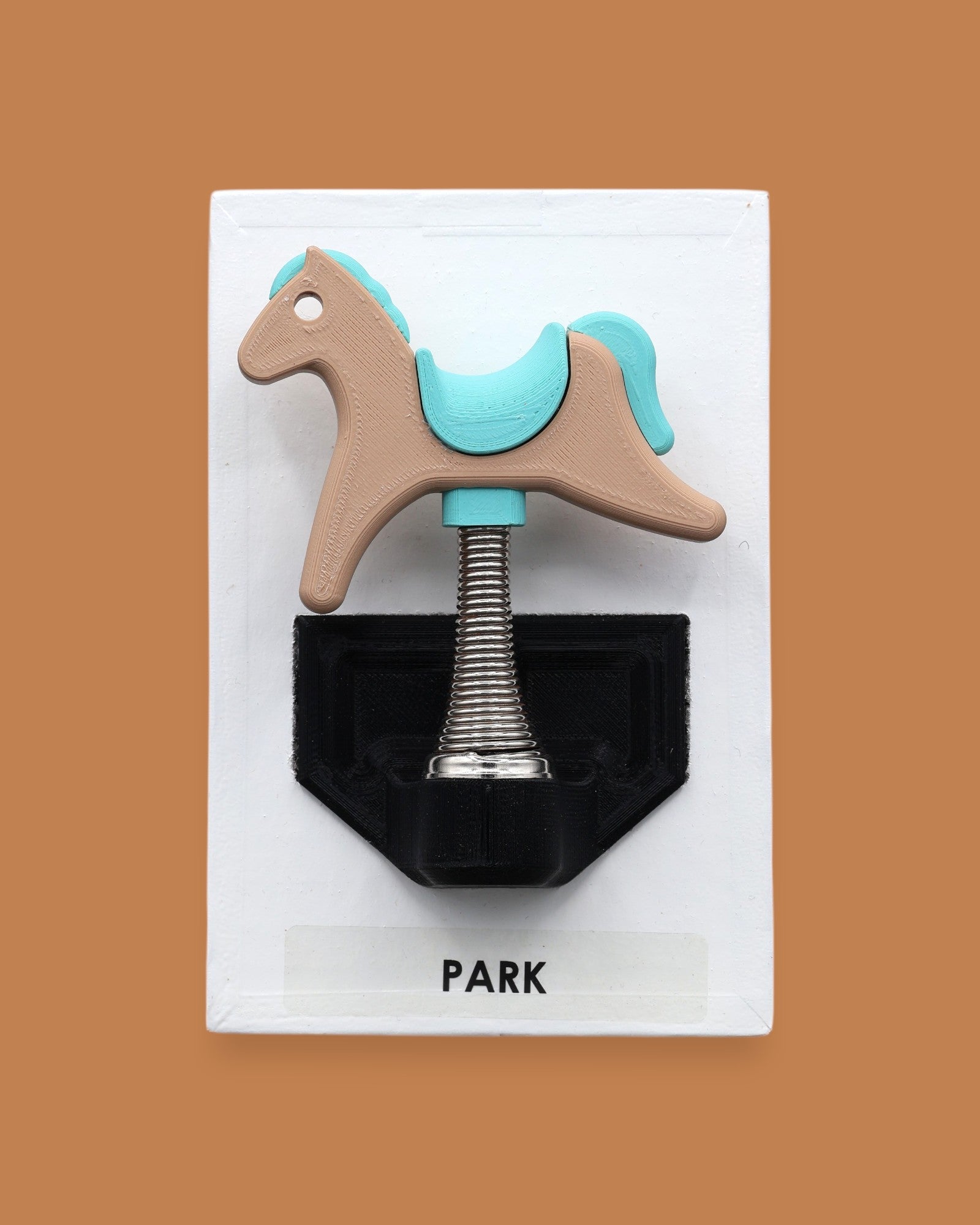 The Park Spring Horse symbol with a 3D printer multicolored spring horse embedded in the center with spring base attached to the horse. Labeled "Park" in black font on white backing at the bottom of the symbol. The background of the symbol is white.