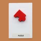 The Puzzle symbol has a red puzzle piece attached in the center. Labeled "Puzzle" in black font at the bottom of the symbol on white backing. The background of the symbol is white.
