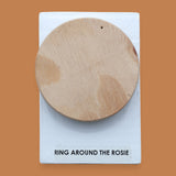 The Ring Around the Rosie symbol has a round wood-like PLA circle that is embedded in the center. Labeled "Ring Around The Rosie" in black font at the bottom of symbol on white backing. The background of the symbol is white.